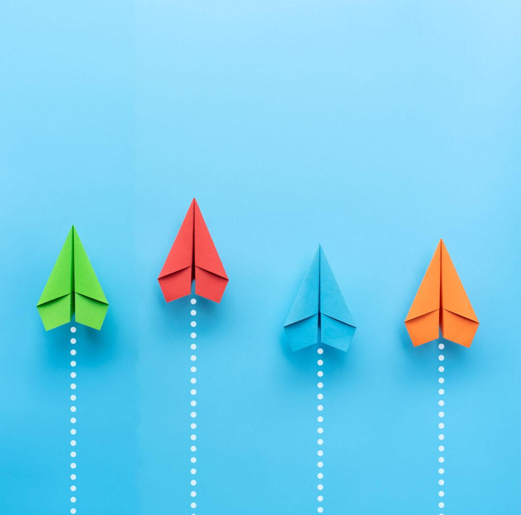 Green, red, blue, orange paper airplanes on blue background