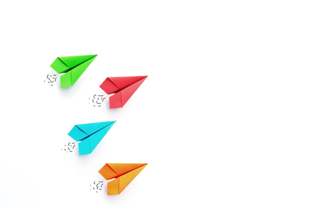 Green, red, blue, orange paper airplanes on white background