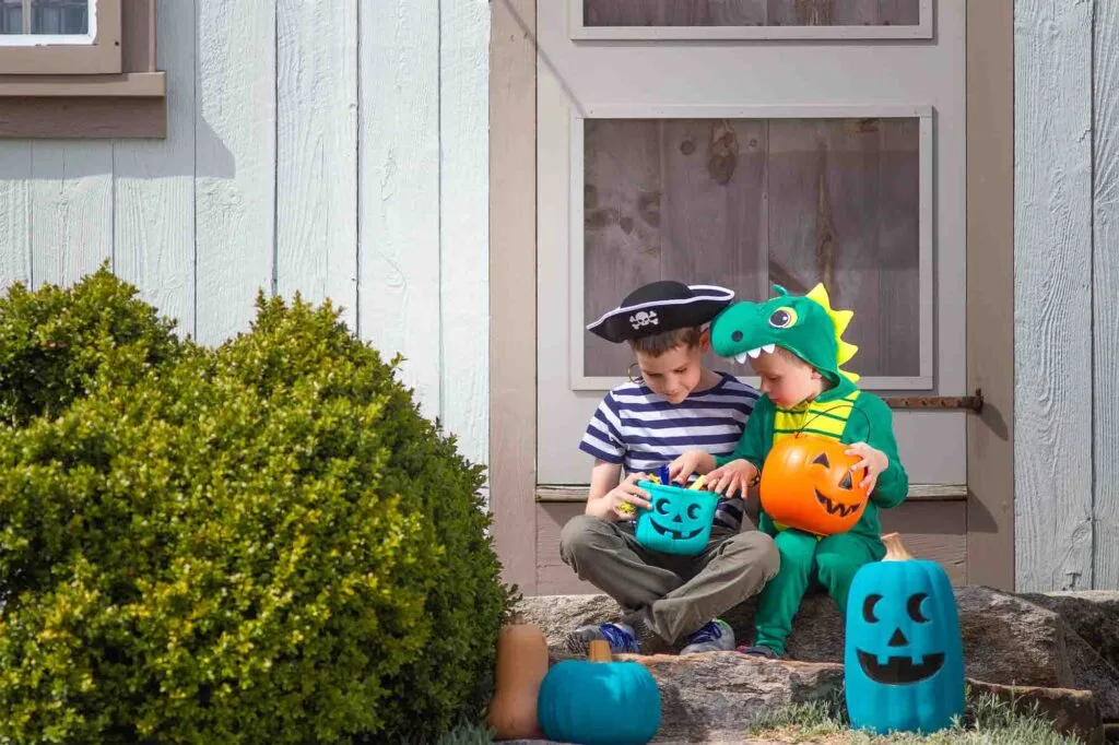Children sitting on porch with orange and teal pumpkins