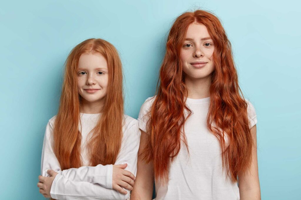 Two girls with orange or red hair against a blue wall