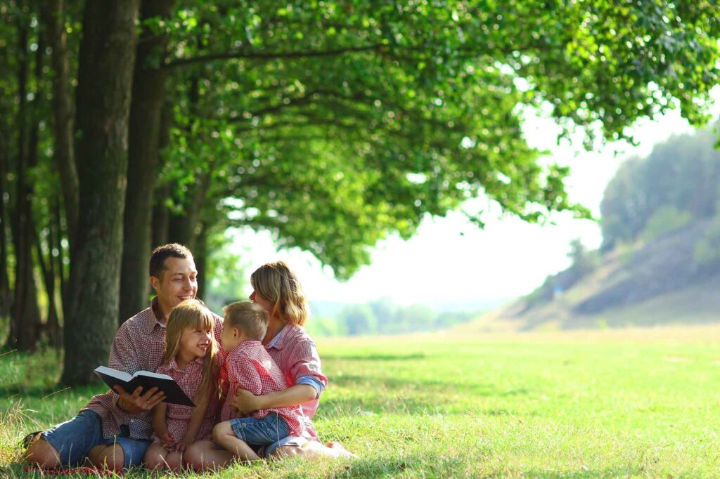 Happy young family reading the Bible while sitting on green grass