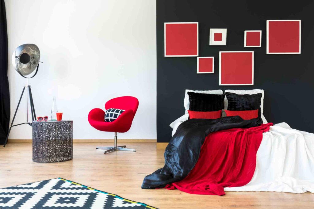 Modern interior with red paintings on black wall above king-size bed with contrast colored pillows