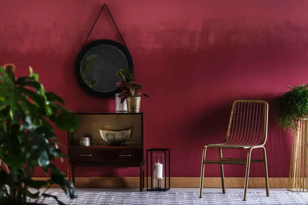 Gold chair next to a cabinet with plant against red wall with mirror in living room