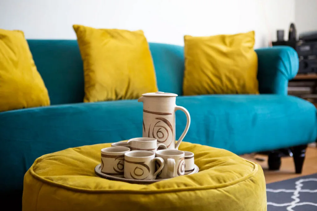 Coffee pot on yellow table and teal couch with yellow pillows