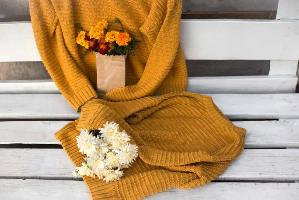 mustard-colored knitted sweaters on a white wooden bench