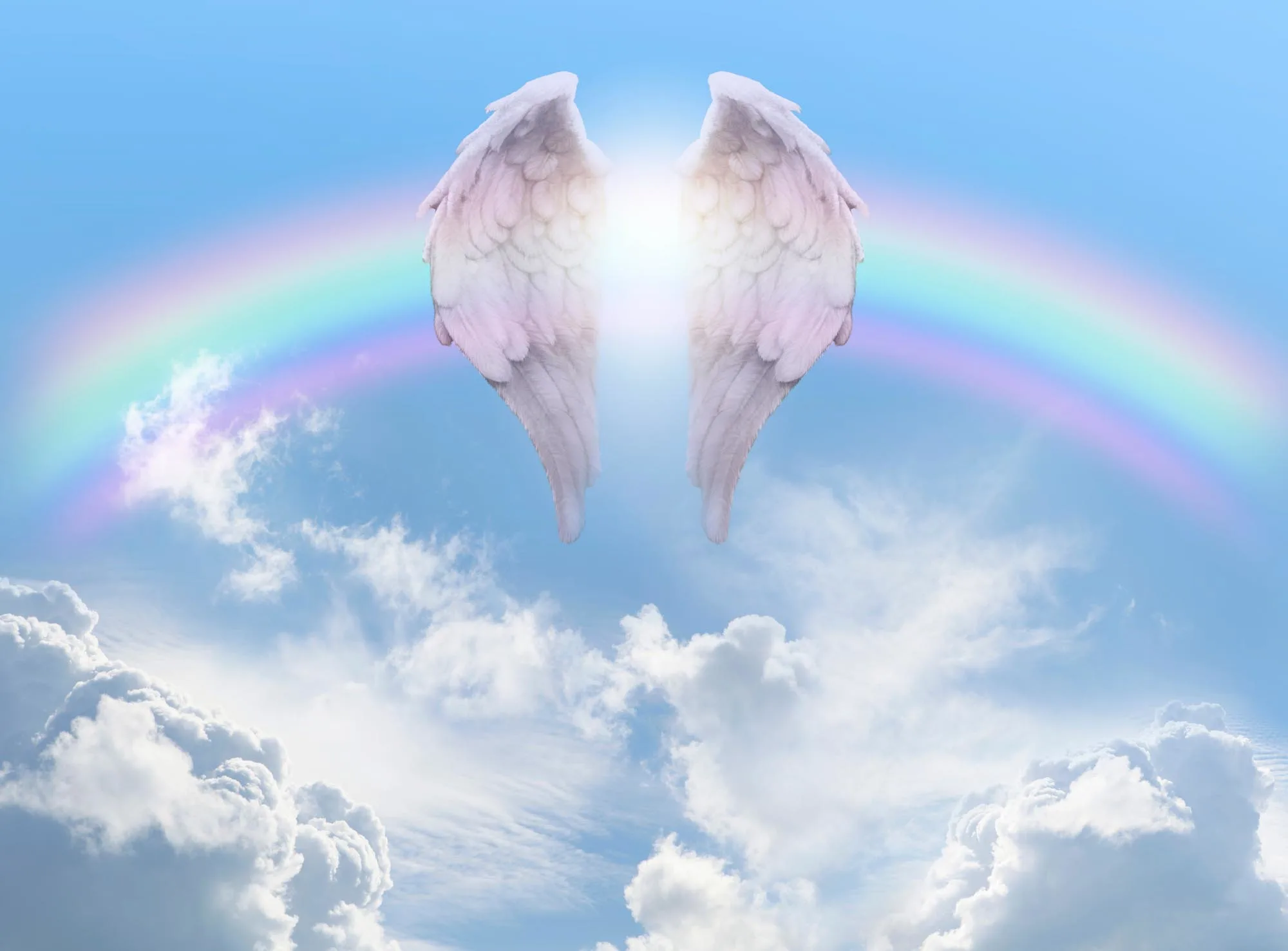 Pair of angel wings in front of a rainbow arc against a beautiful blue sky