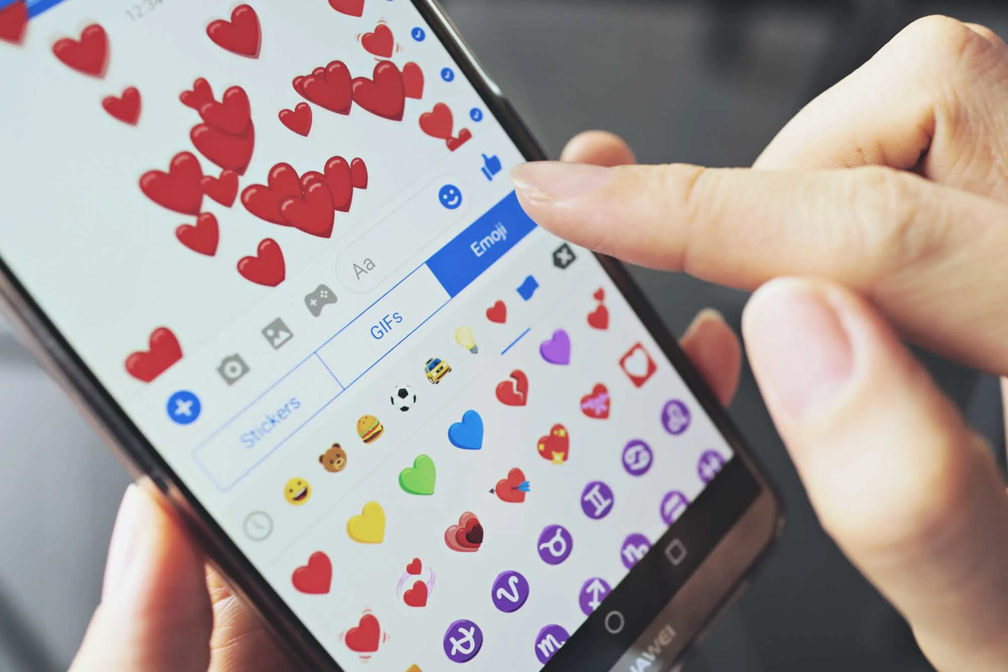 Woman holding smartphone and sending colorful heart emoji on screen